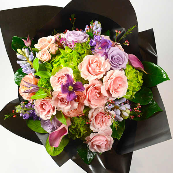 Bouquet of pink and lavender roses with green hydrangeas in black wrap