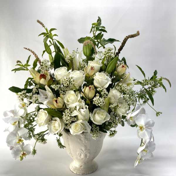 White roses and orchids arranged in a white urn vase