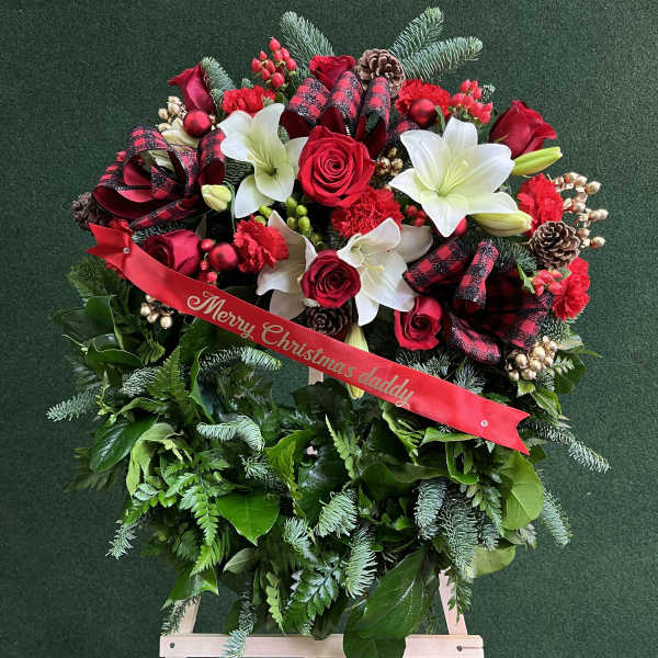 Christmas floral wreath with red roses, white lilies, and a ribbon on an easel