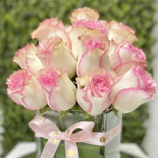 Compact arrangement of white roses edged in pink in a square glass vase with a pink ribbon bow