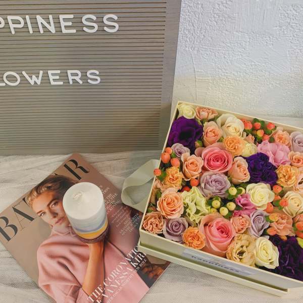Box of pastel roses with a candle and magazine beside a flower sign