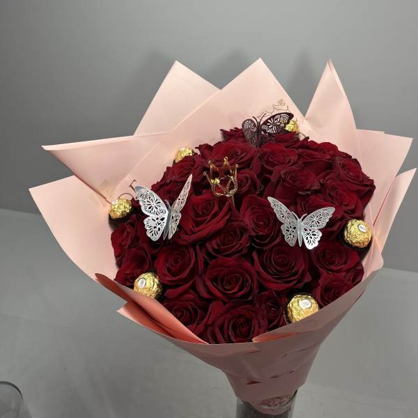 Bouquet of red roses wrapped in pale pink paper with chocolate candies and butterfly picks