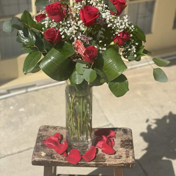Red roses in a clear glass vase with baby's breath and rose petals