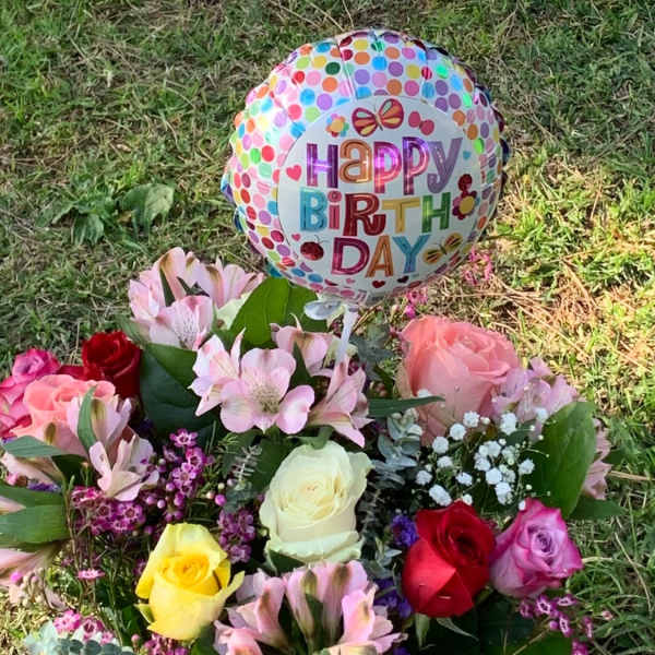 Birthday balloon above a colorful rose bouquet on grass