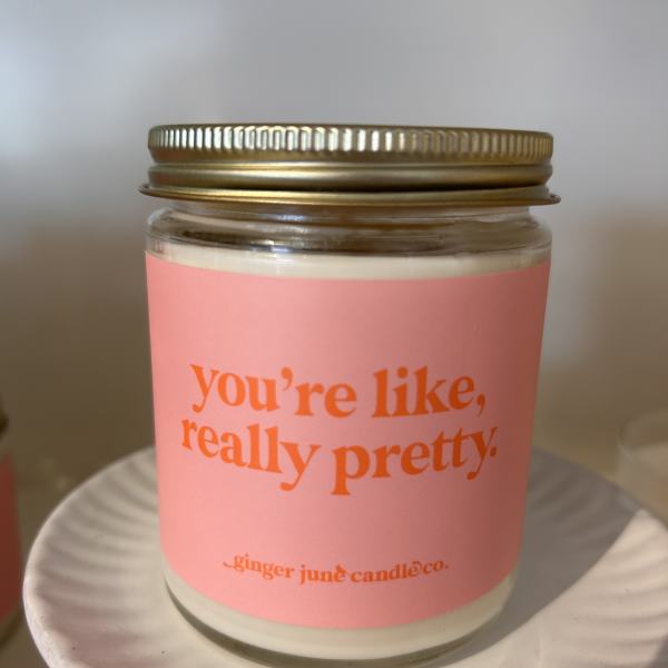 Pink-labeled jar candle with gold lid on a white ceramic pedestal stand
