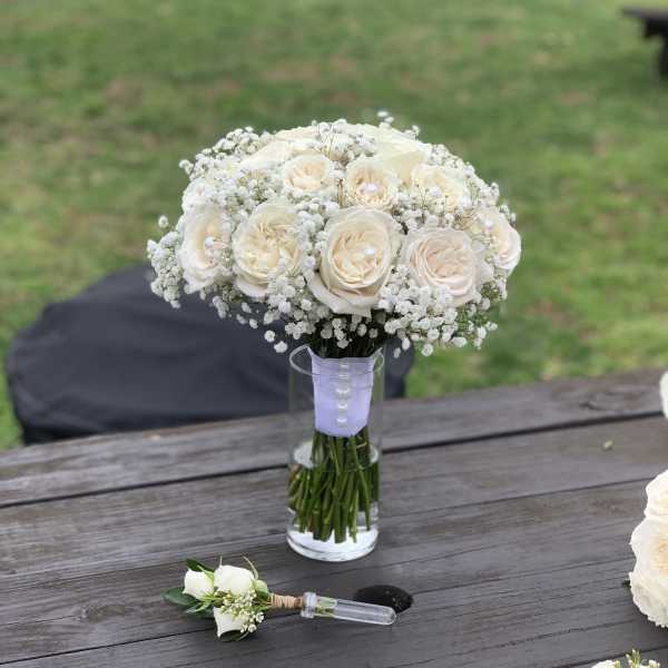 Cream rose bouquet in a glass vase with a matching boutonniere on a table