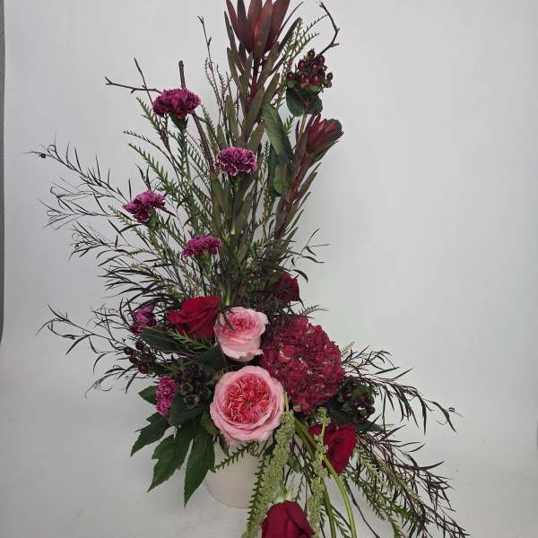Tall floral arrangement with pink and red roses in a white vase