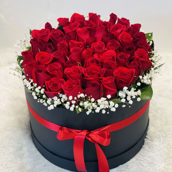 Red roses arranged in a round black box with a red ribbon.