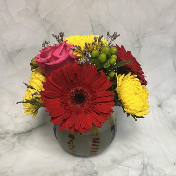 Bouquet of red gerbera daisies, yellow mums, and a pink rose in a round vase