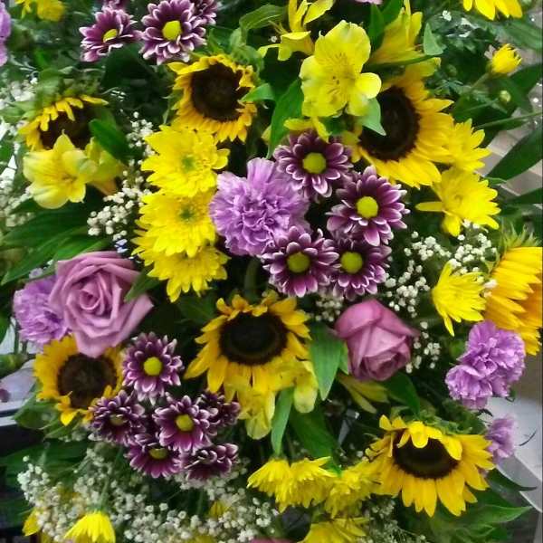 Bouquet of yellow sunflowers, purple roses, and purple daisies