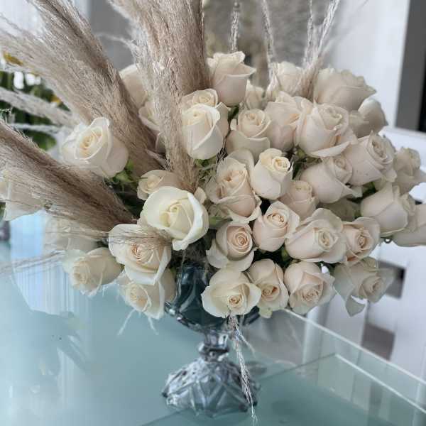 Cream rose bouquet with tall pampas grass in a glass vase