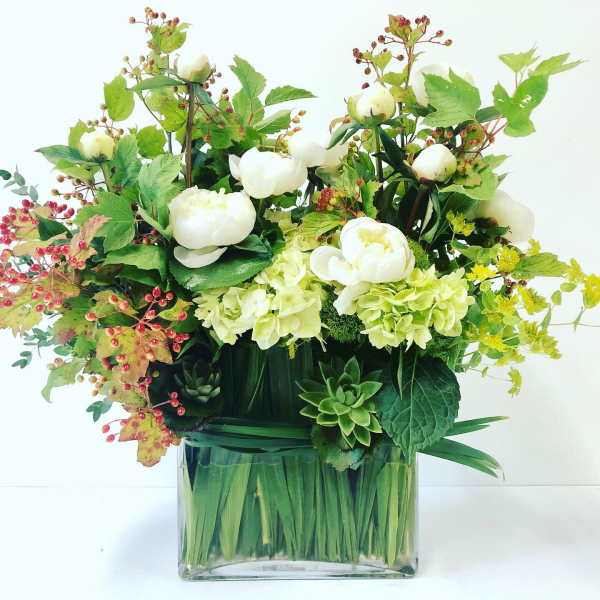 White flowers in a clear square vase with green foliage and red berry accents