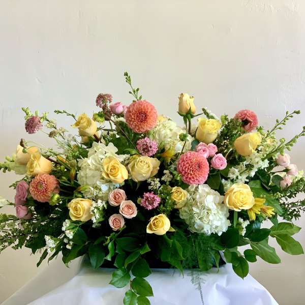 Large pastel floral arrangement with roses, dahlias, and hydrangeas in a low container