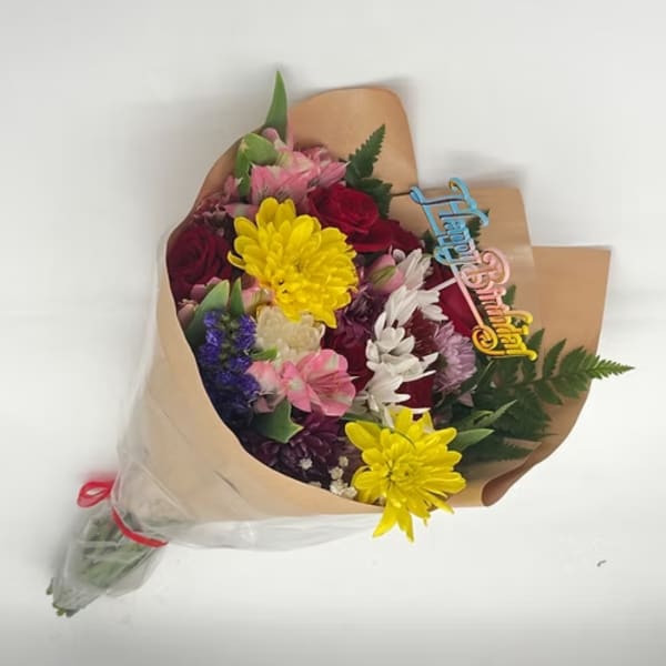 Mixed bouquet of colorful flowers wrapped in brown paper with a birthday topper