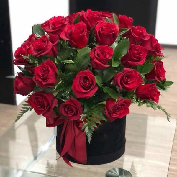 Red roses arranged in a black hatbox with a red ribbon