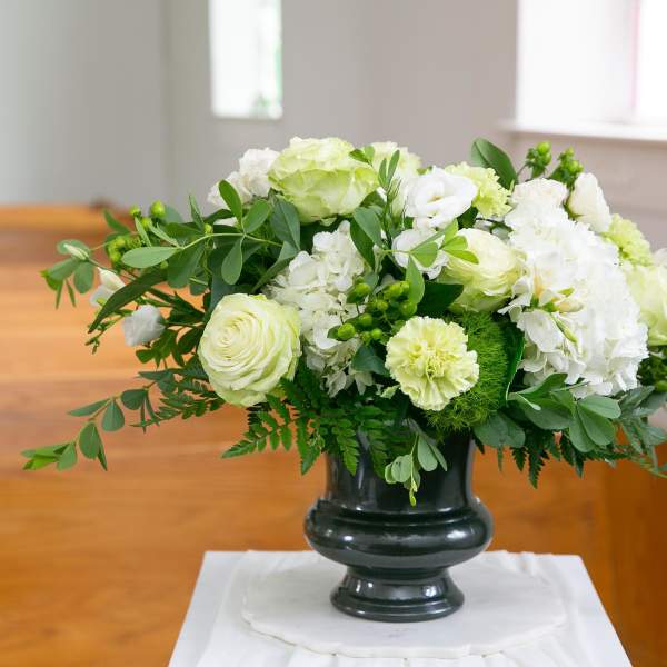 White and pale green floral arrangement in a dark vase