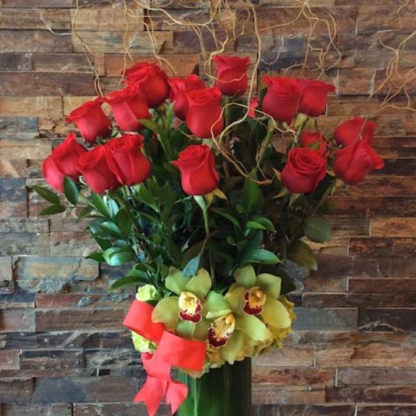 Red roses and yellow orchids in a tall glass vase with a pink ribbon