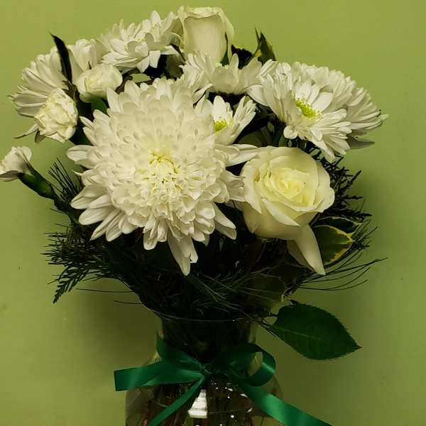 White flowers arranged in a glass vase with a green ribbon