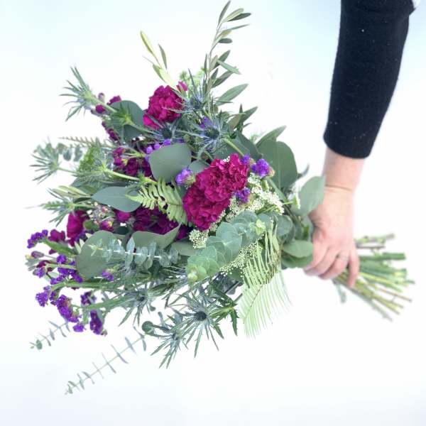 Handheld bouquet of magenta and purple flowers with mixed greenery