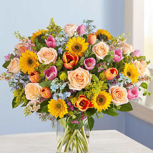 Mixed bouquet of roses, tulips, and sunflowers in a glass vase