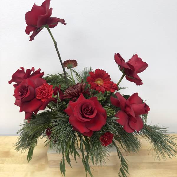 Red roses and mixed red flowers in a low arrangement with pine greenery