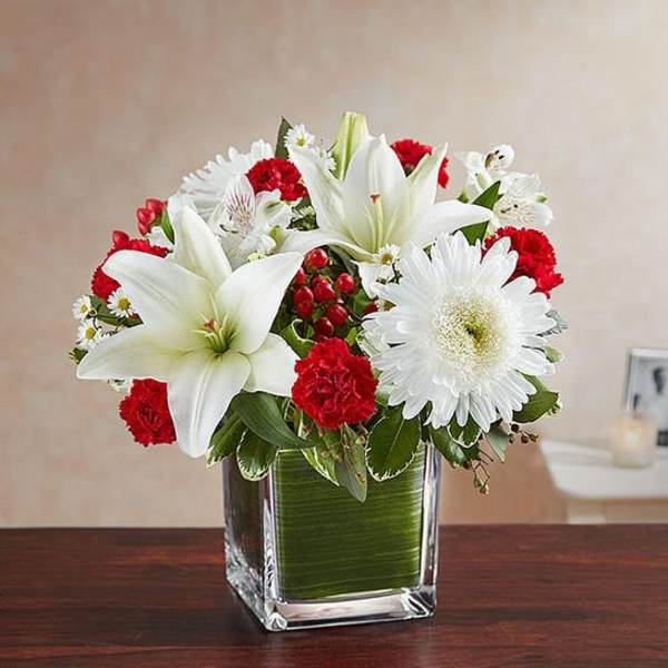 White lilies and daisies with red carnations in a glass vase