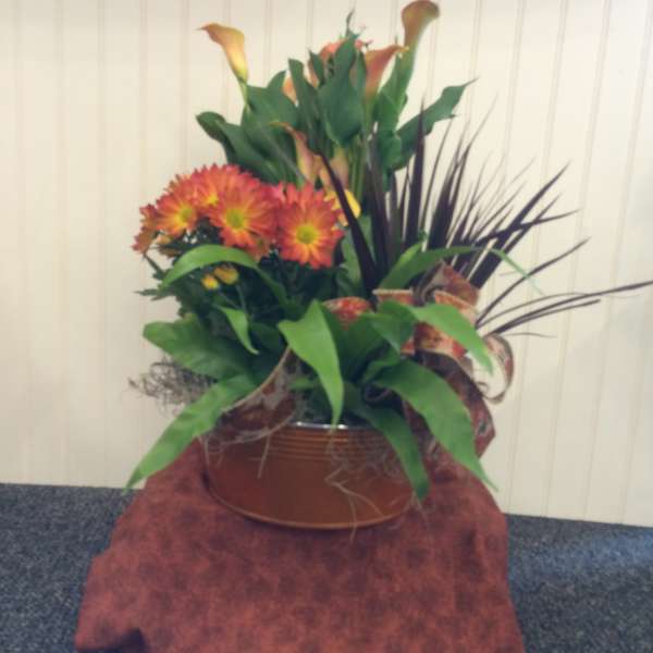 Orange chrysanthemums and calla lilies in a copper-toned container