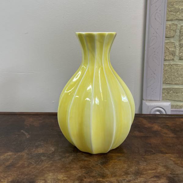 Yellow ceramic vase with a fluted neck on a wooden surface