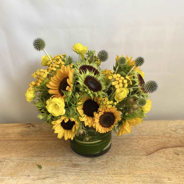 Yellow sunflowers and roses arranged in a green glass vase