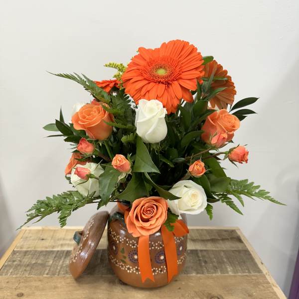 Orange gerbera daisies and roses arranged in a painted ceramic pot