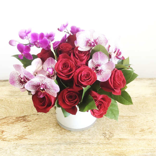 Red roses and pink orchids arranged in a white vase