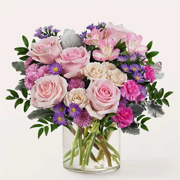 Bouquet of pink roses, alstroemeria, and purple daisies in a clear glass vase