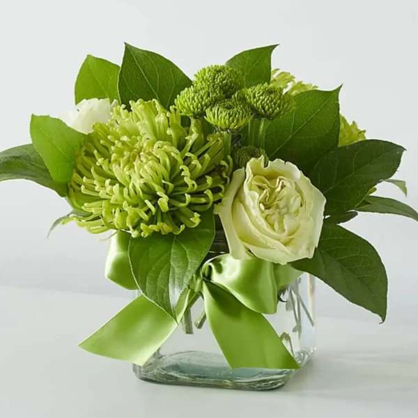 Green and white floral arrangement in a clear glass vase with a ribbon
