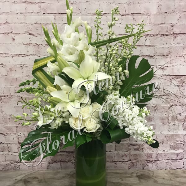 White floral arrangement in a tall green vase with large tropical leaves