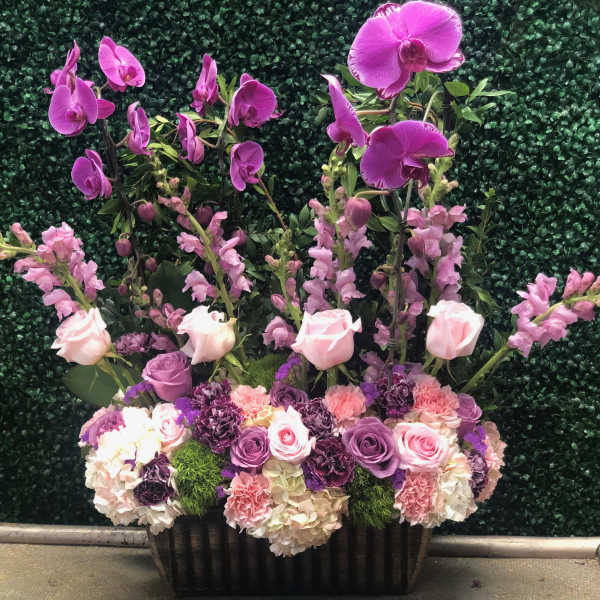 Tall floral arrangement with pink orchids, roses, and snapdragons in a black container