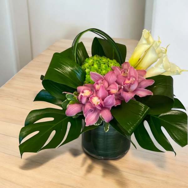 Pink orchids and white calla lilies in a dark vase with large tropical leaves