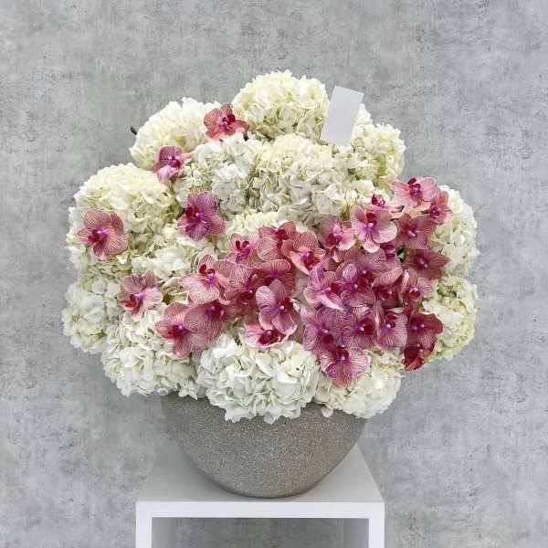 White hydrangea arrangement with pink orchids in a gray vase
