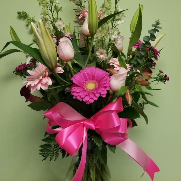Tall bouquet of pink lilies, gerbera daisies, and a bright ribbon in a glass vase