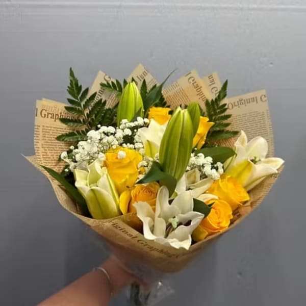 Handheld bouquet of yellow roses and white lilies wrapped in paper