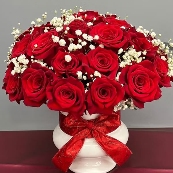 Red roses and white baby's breath in a white vase with a red ribbon