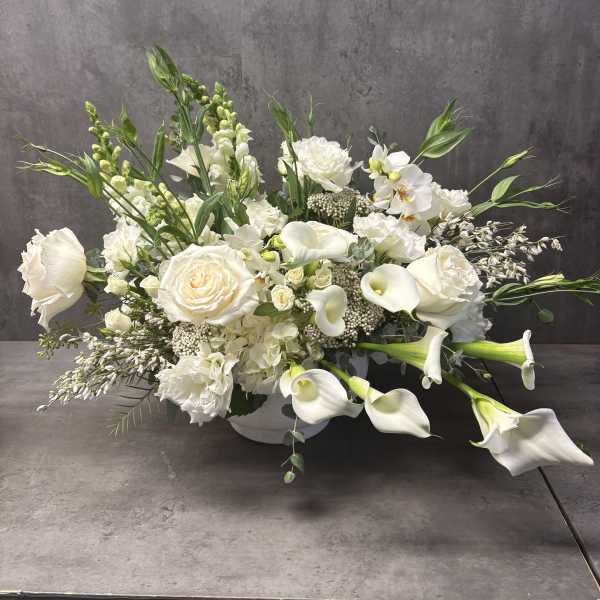 White floral arrangement with roses, calla lilies, and orchids in a low vase