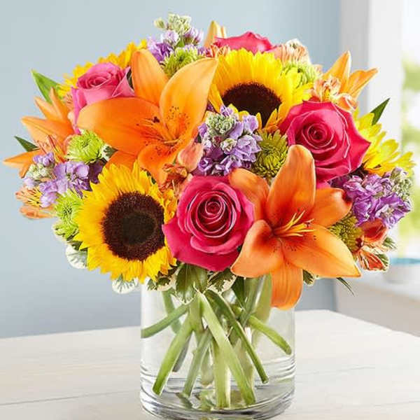 Bright mixed bouquet with sunflowers, roses, and lilies in a glass vase