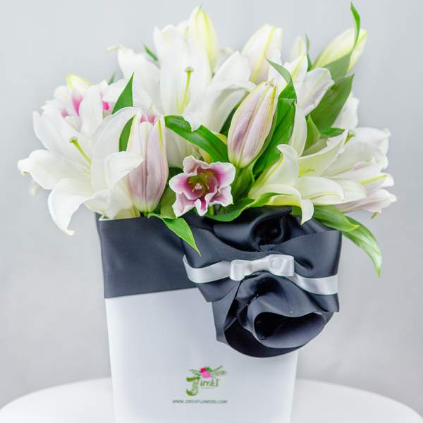 White lilies arranged in a white box with a black ribbon