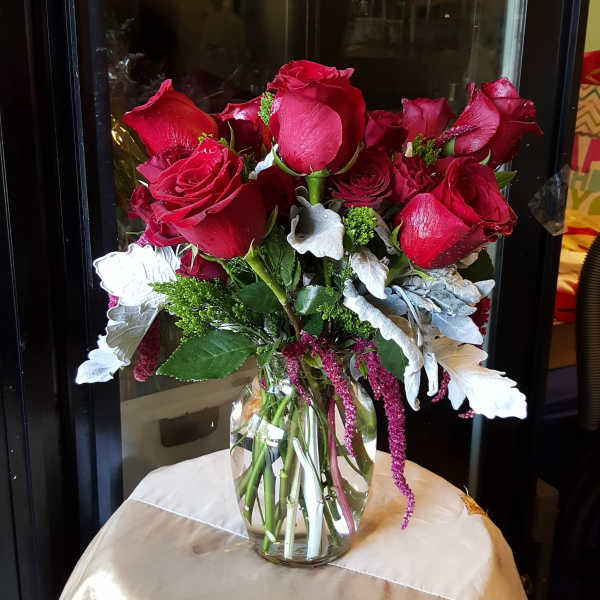 Red roses arranged in a clear glass vase with silver foliage