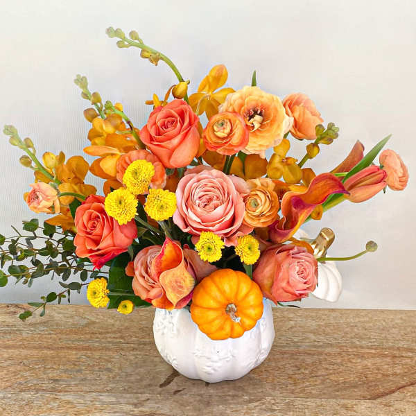 Orange and pink floral arrangement in a white pumpkin vase