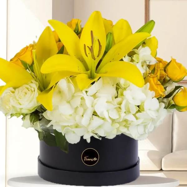 Yellow lilies and white hydrangeas in a black round box with yellow roses
