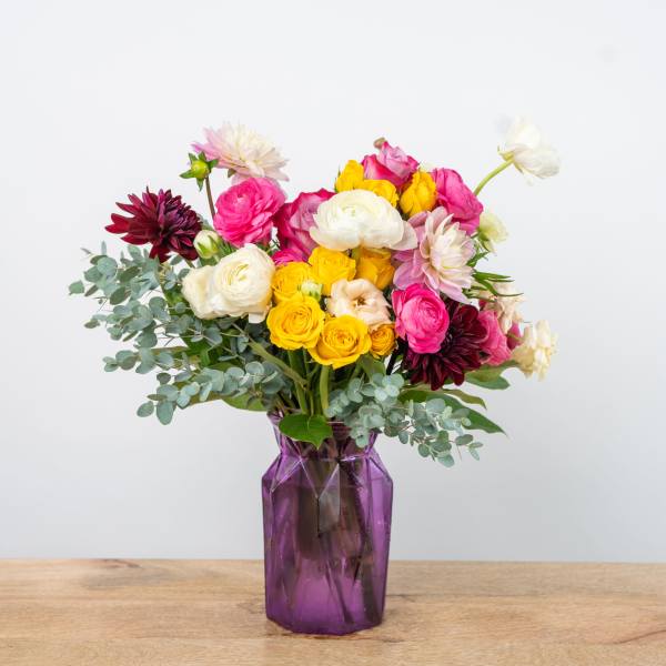 Mixed bouquet of pink, yellow, white, and burgundy flowers in a purple vase