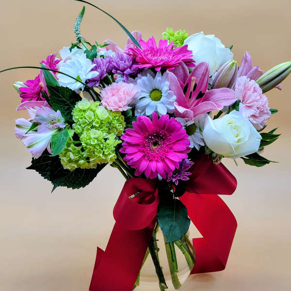 Mixed bouquet of pink, white, and green flowers in a glass vase with a red ribbon