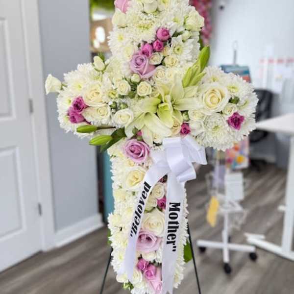 Cross-shaped floral tribute with white and pink flowers on a stand