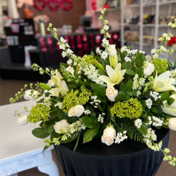 Large white and green arrangement with roses, lilies, and hydrangeas on a black-draped stand